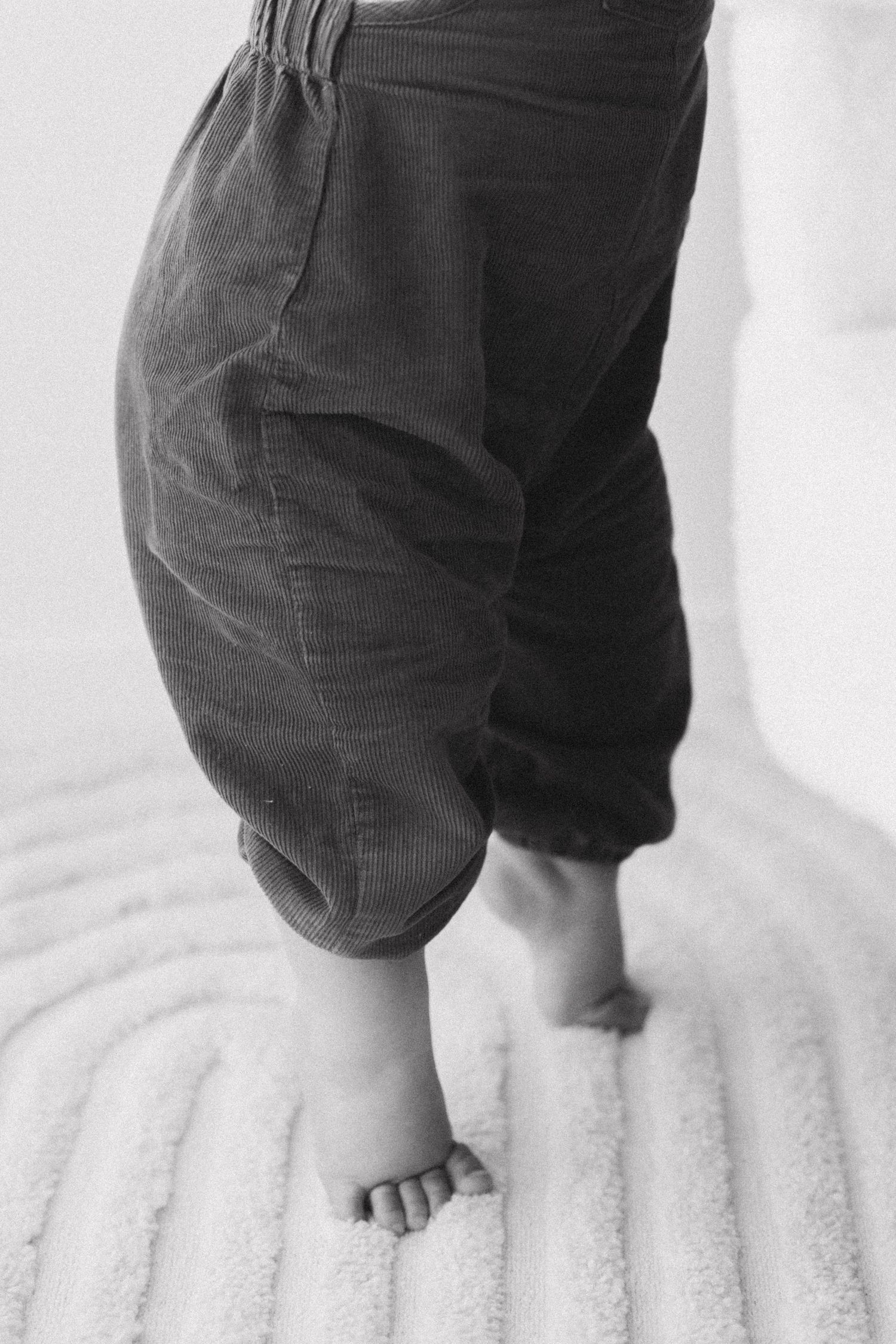 A series of black and white photos showing small bare feet walking on a soft white surface.