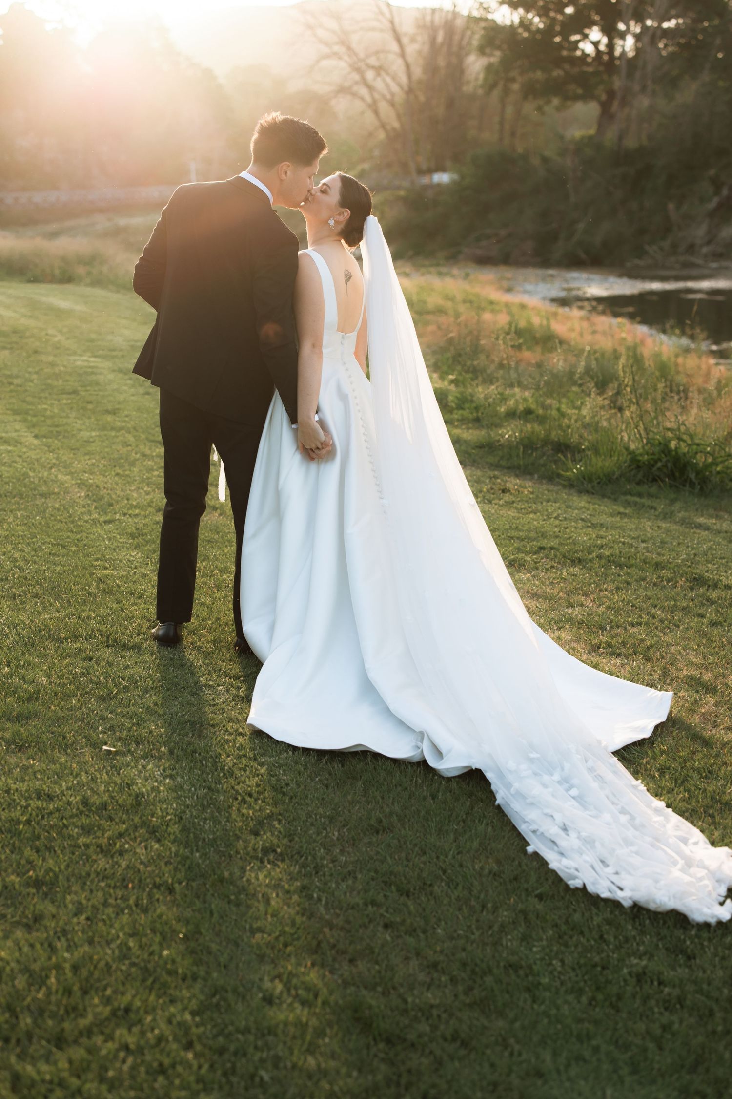 Newlyweds walk together at sunset across a grassy field with flowing white dress.