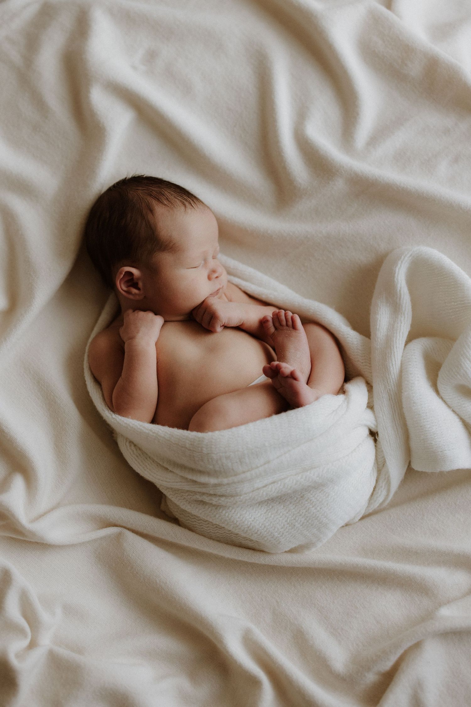 Serene newborn baby wrapped in white blanket sleeping peacefully on soft textured bedding.