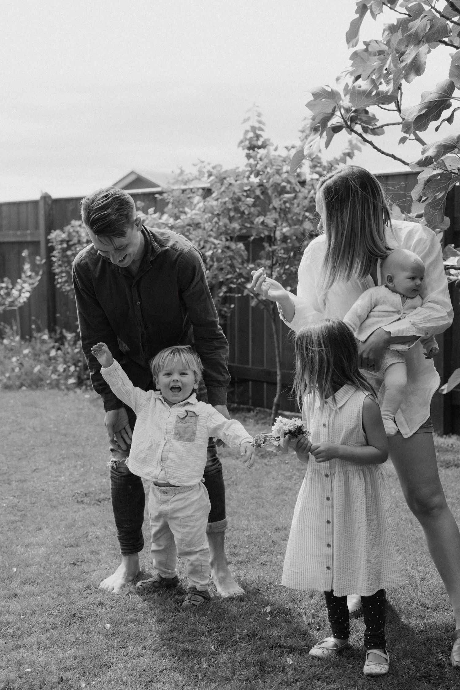 Family plays together outdoors in black and white, creating sweet candid moments in a garden setting.