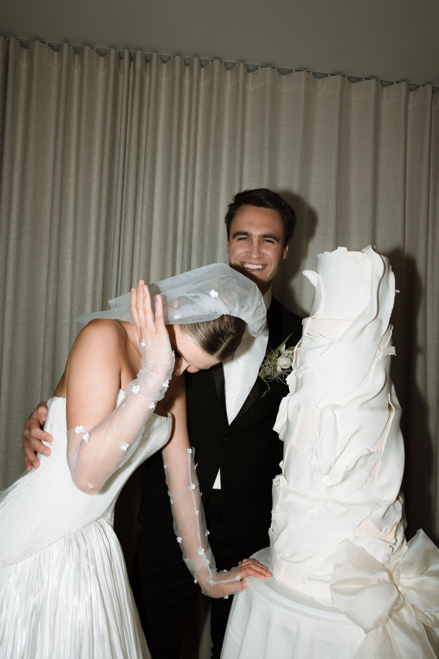 Candid wedding moments show playful interaction in front of light curtains.
