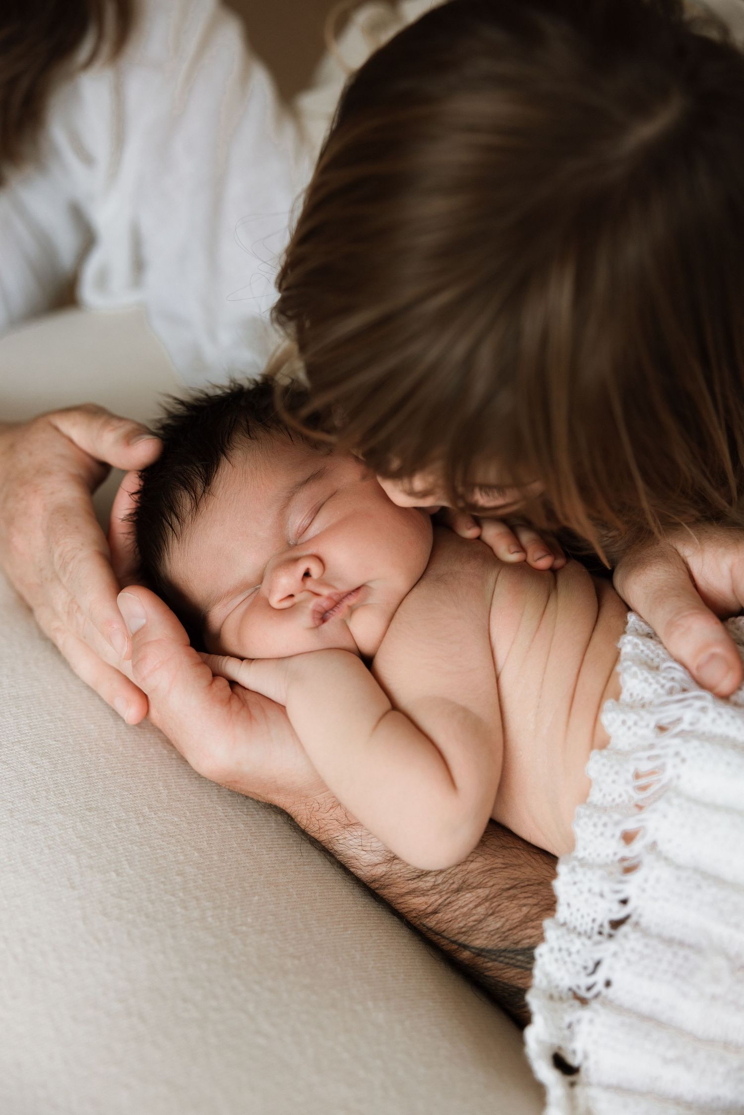 Sleeping newborn baby cradled in gentle hands with soft intimate lighting.