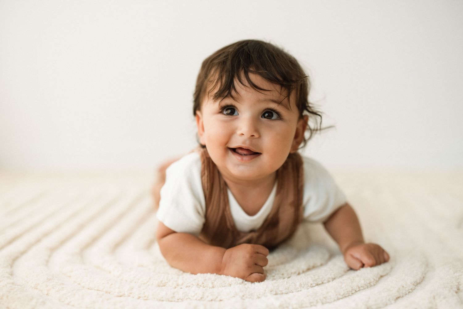 Joyful baby crawling on white surface during photography session.