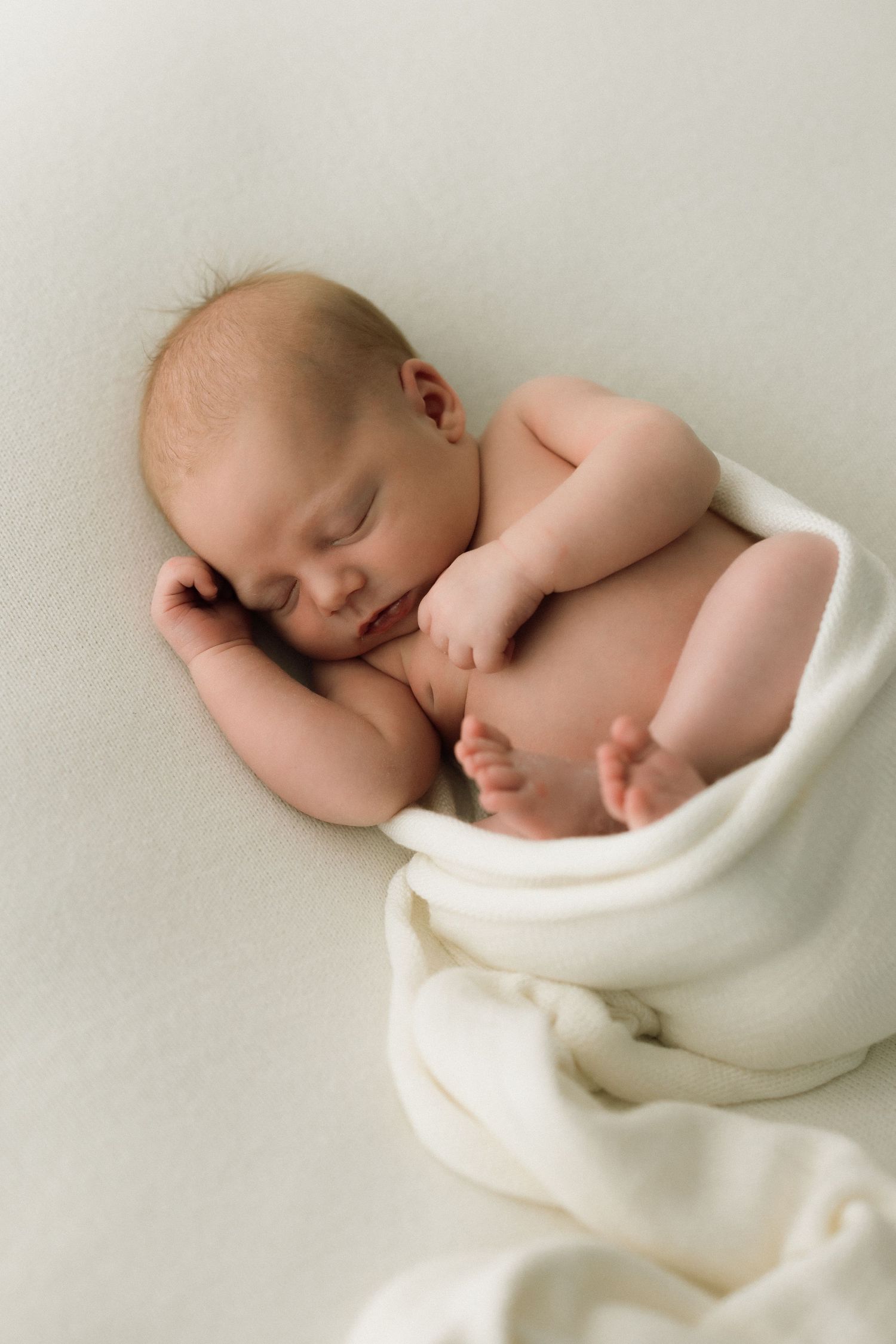 Minimalist portrait of sleeping newborn wrapped in cream-colored fabric.