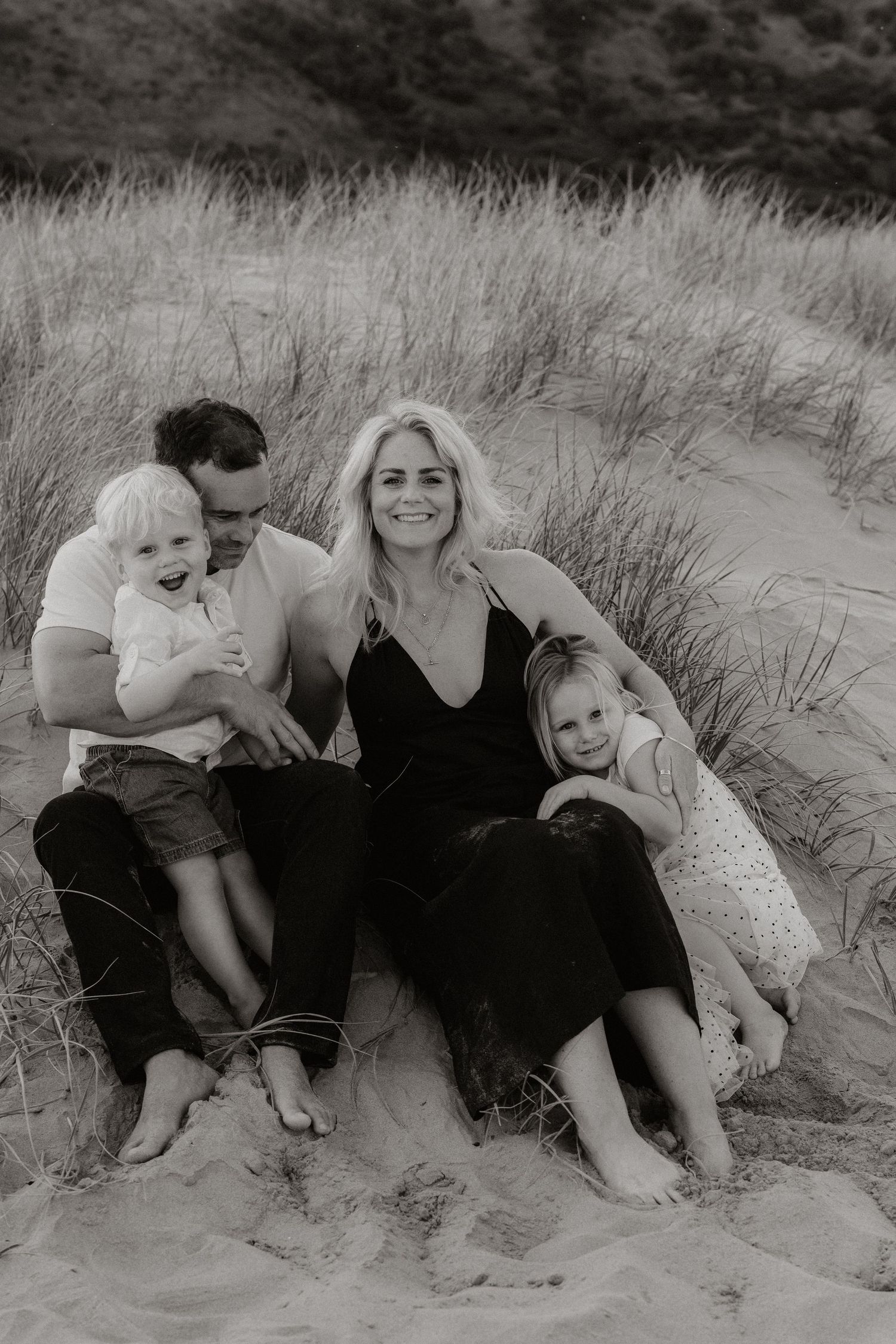 Black and white photoshoot on sandy beach dunes showing candid family moments together.