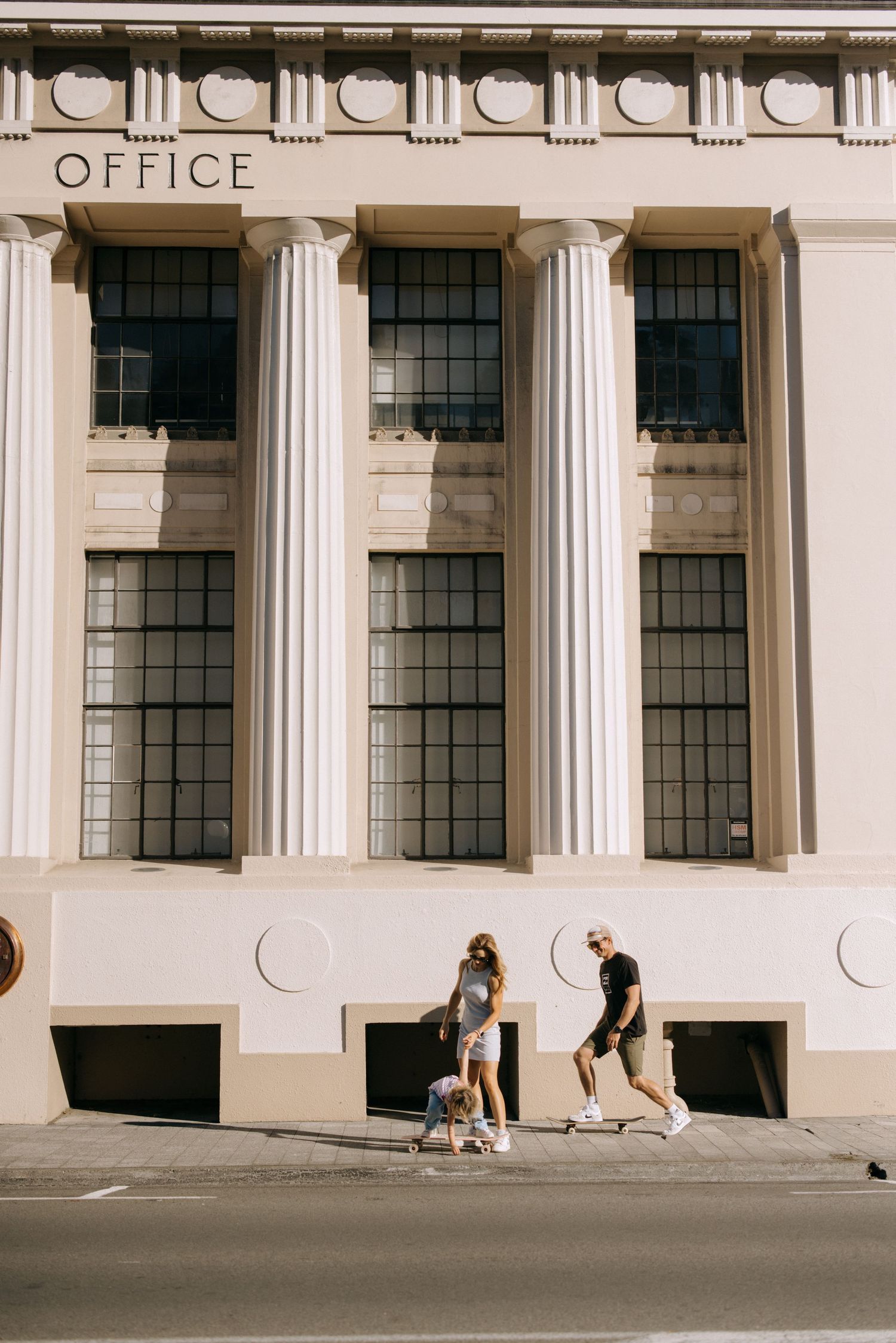 Two skateboarders practicing tricks in front of a classical building with white columns.