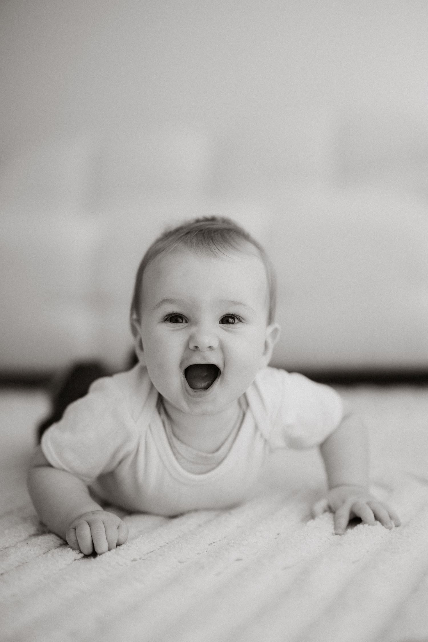 Black and white series of smiling baby lying on plush white surface.