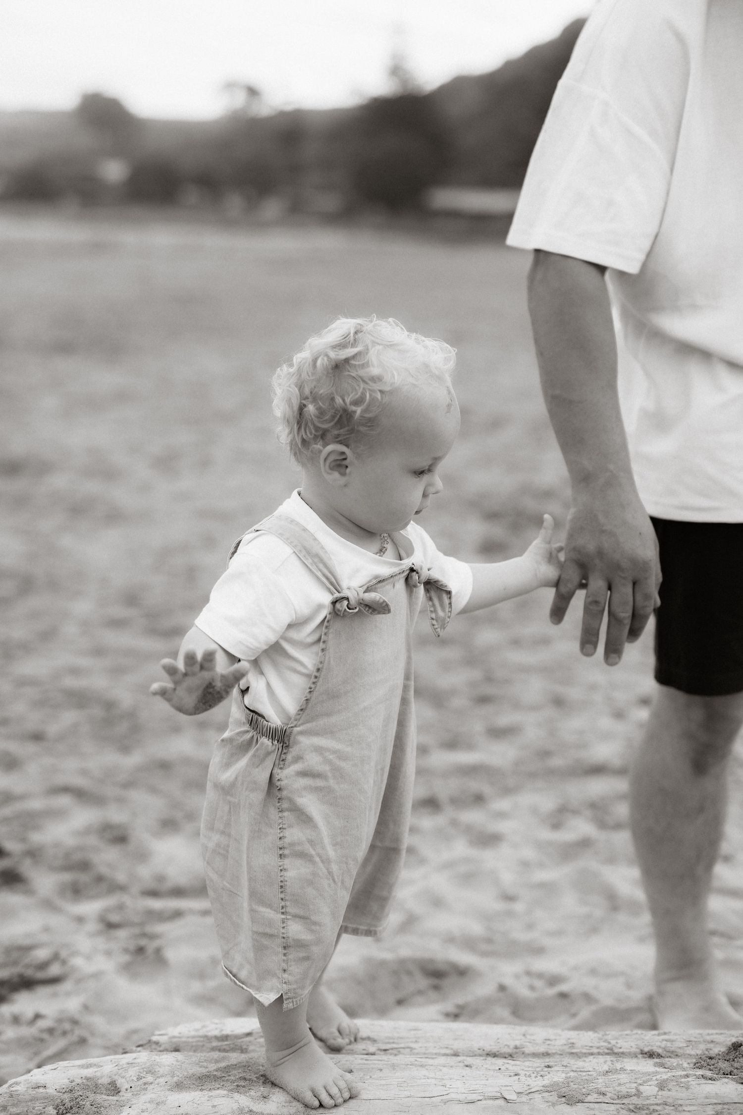 Black and white vintage sequence showing a small child in white clothing walking in sand near an adult's legs.