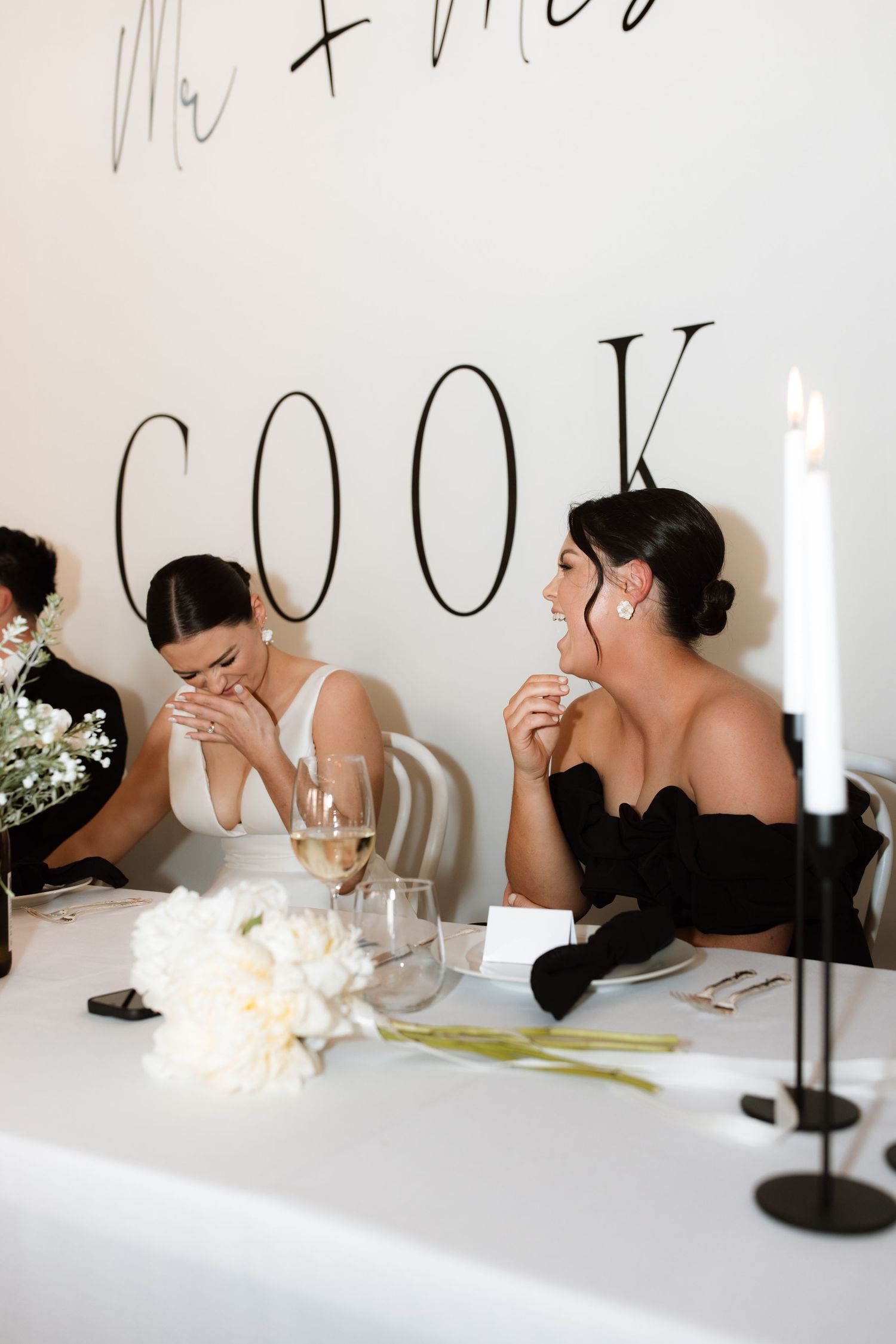 Intimate wedding reception moment captured at white table with decorative text wall.