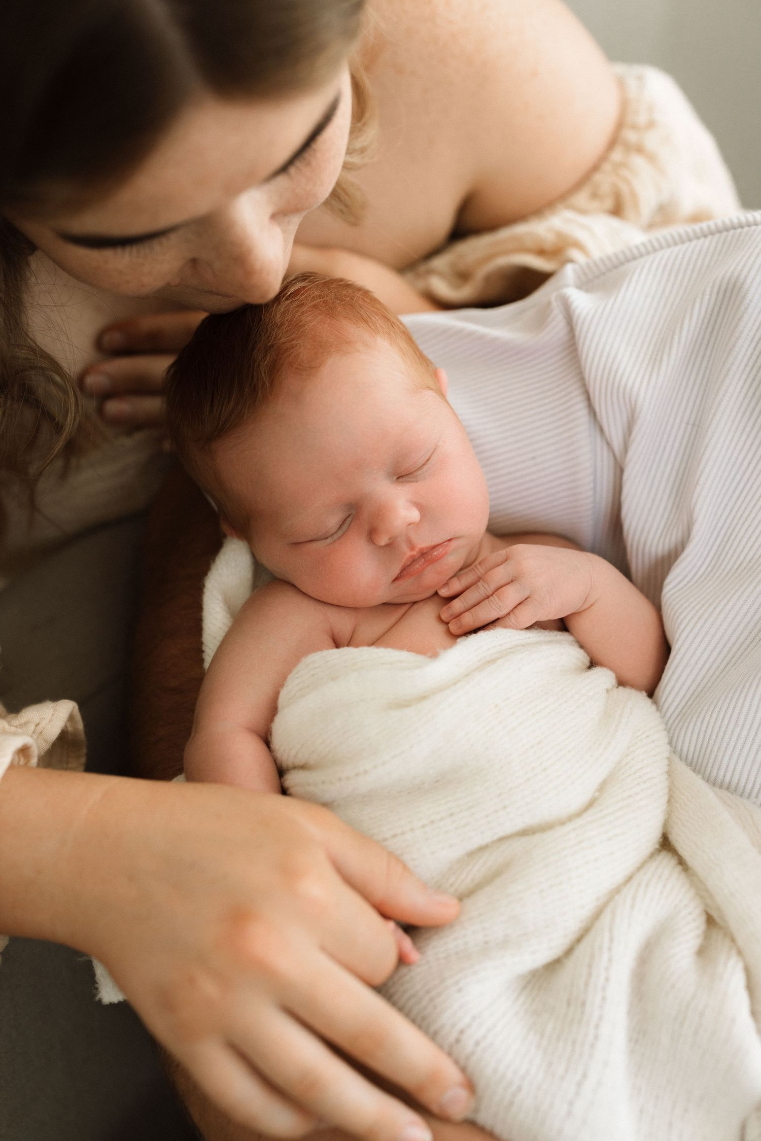 Peaceful sleeping baby swaddled in white being held close in intimate portrait.