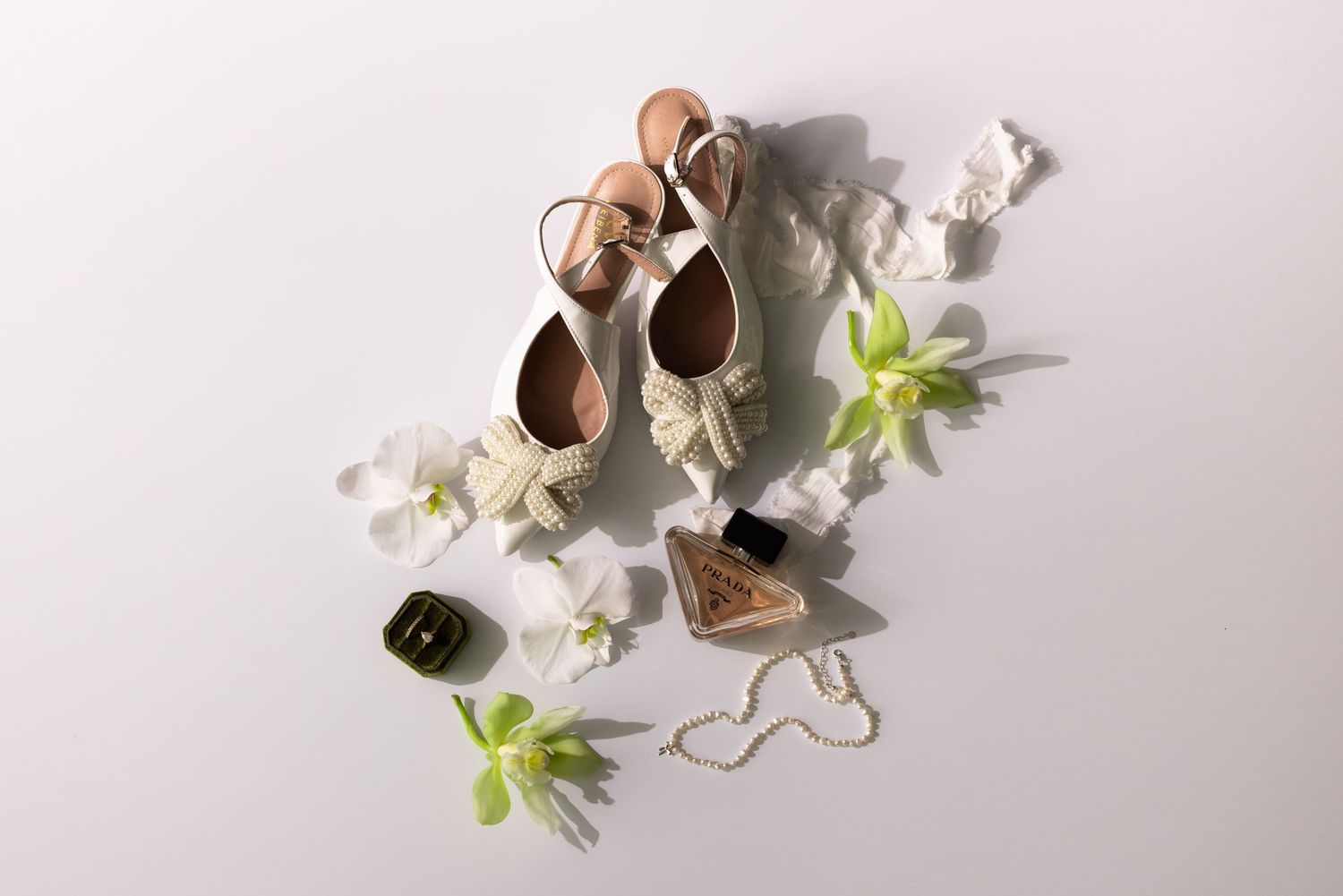 Flat lay of nude ballet shoes with delicate white flowers and greenery on light background.
