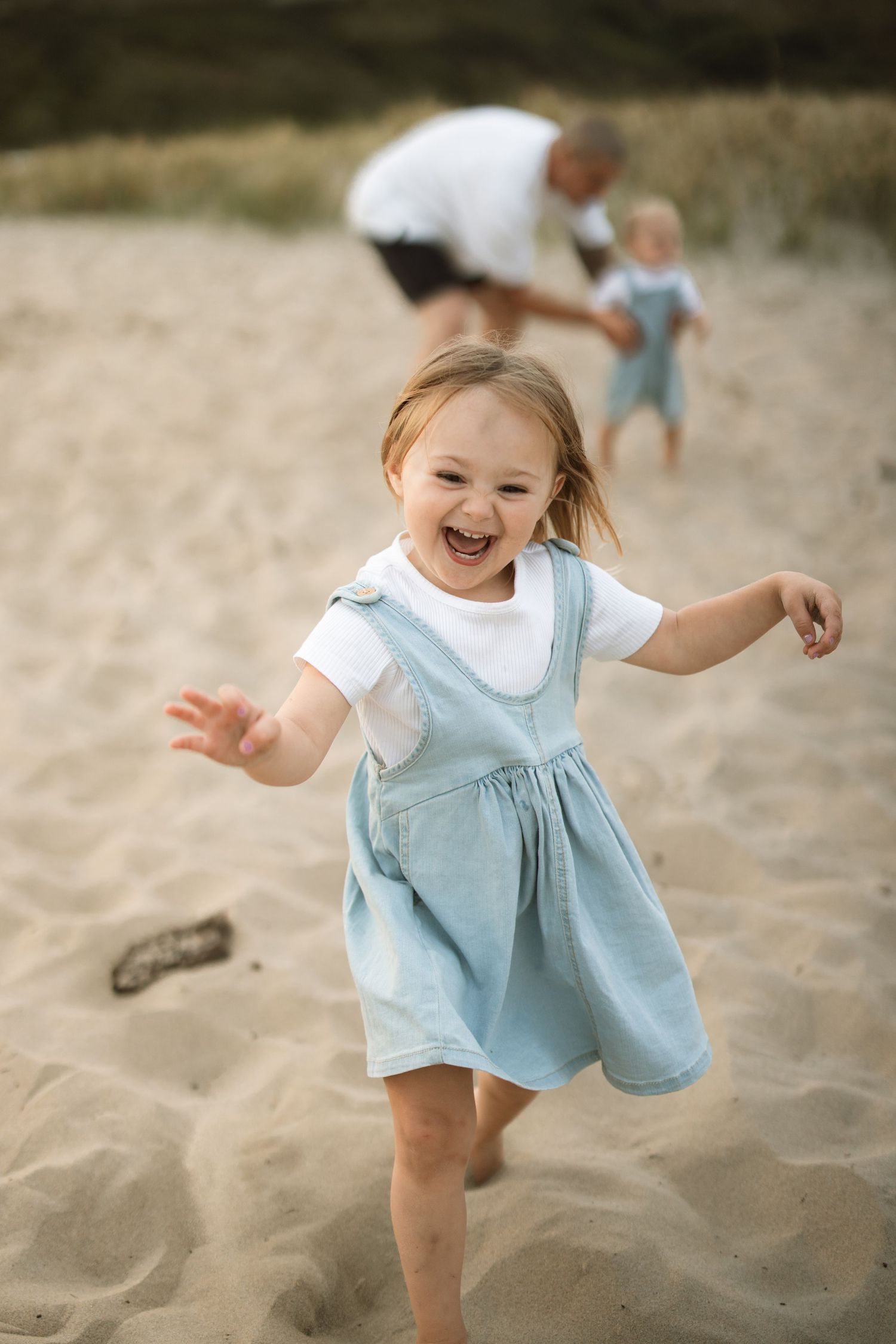 A child in a light blue dress runs and plays joyfully on a sandy beach.