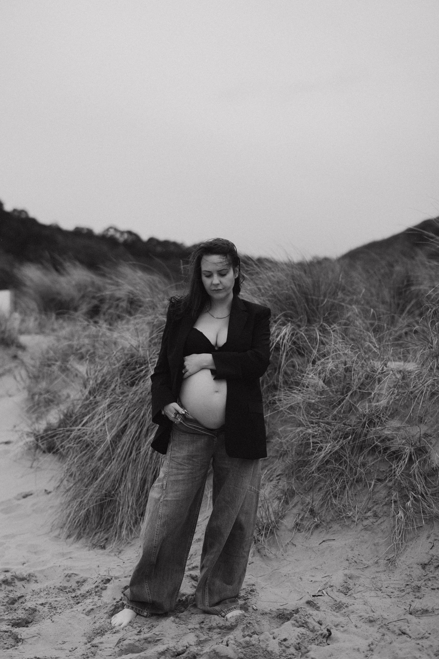 A black and white maternity portrait on windswept sand dunes.