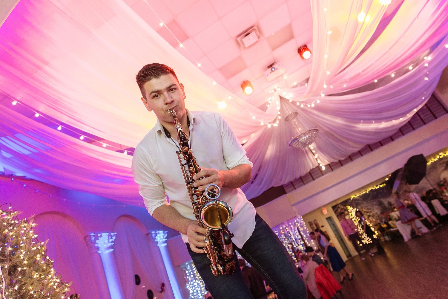 Saxophone performer playing at an elegant event with pink and purple lighting.