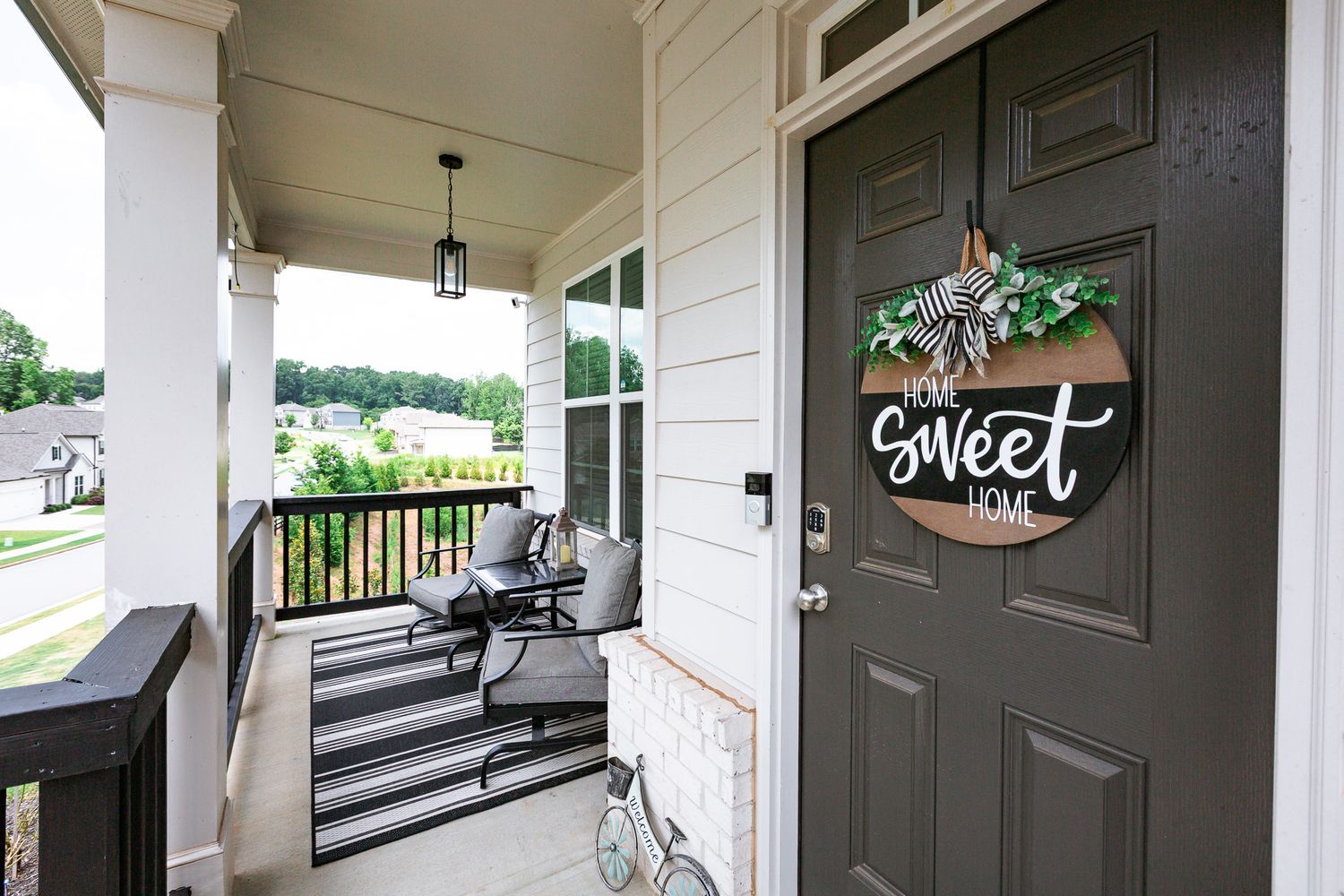Covered front porch with dark door featuring 'Sweet Home' wreath decoration and outdoor seating.