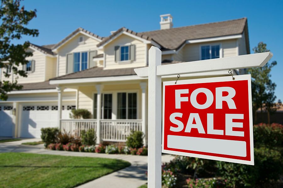 Row of residential homes with For Sale signs in front yards on sunny day.