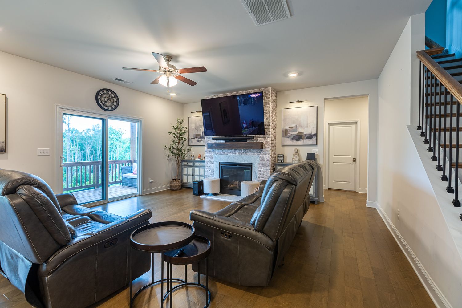 Large living room with dark leather furniture, ceiling fan, and natural lighting from windows.