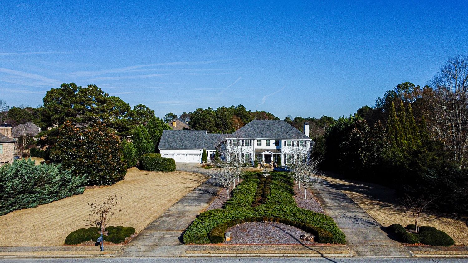 Aerial view of a grand white estate home with circular driveway and manicured landscaping.