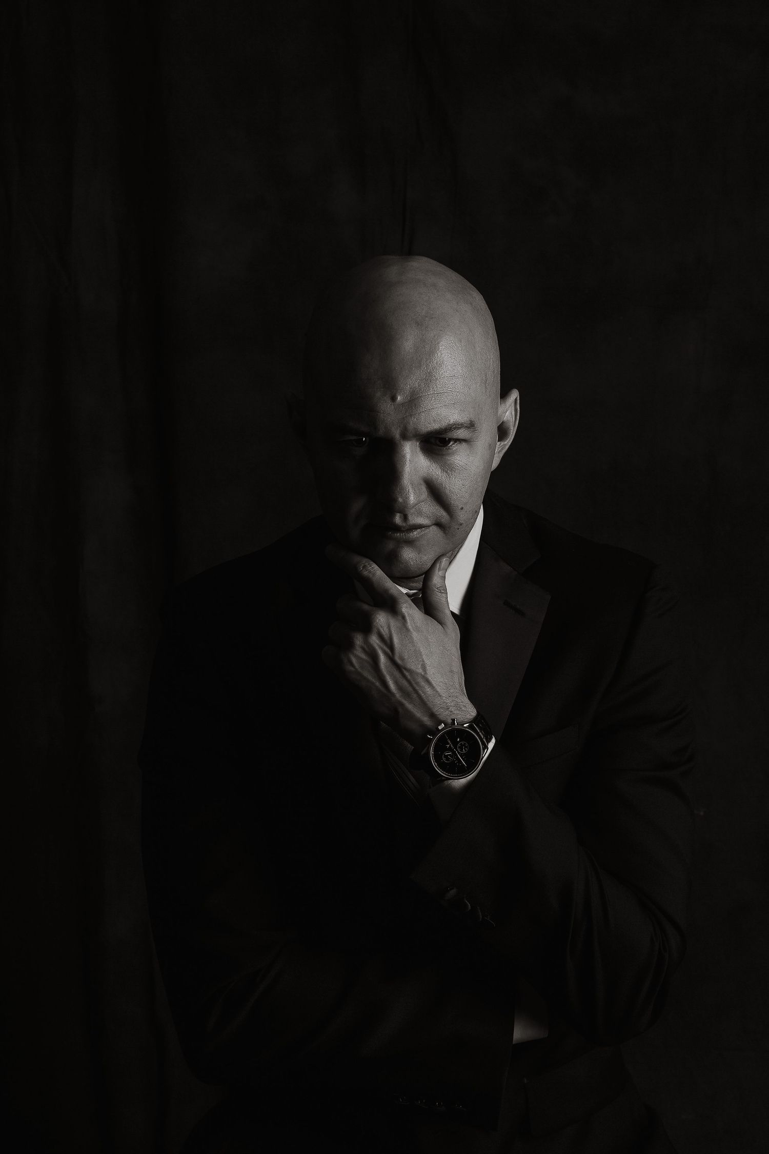 Dramatic black and white portrait of person in suit with contemplative expression.