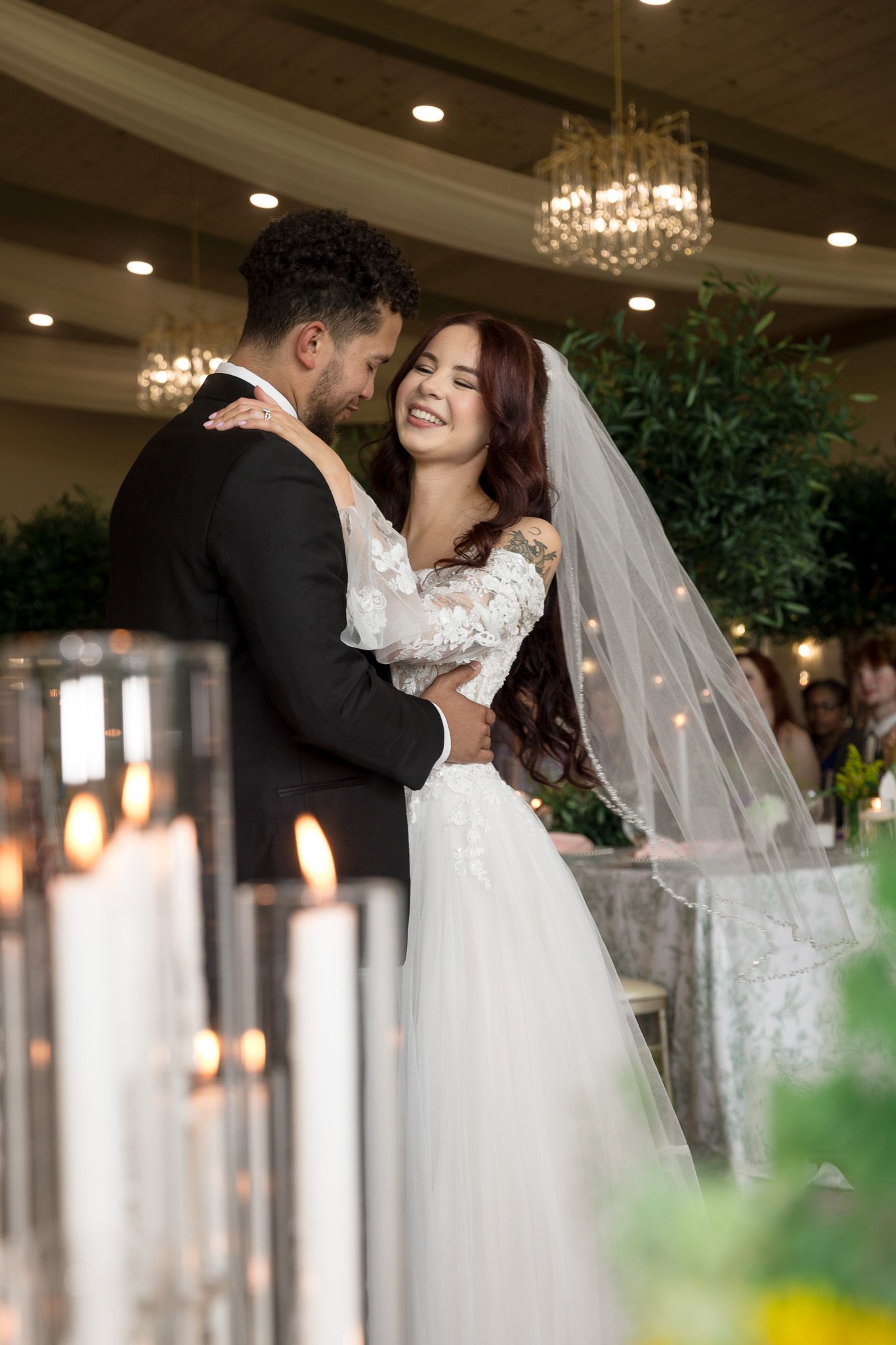 A joyful bride in a white lace gown and veil embraces her groom in a suit at an elegant candlelit wedding.