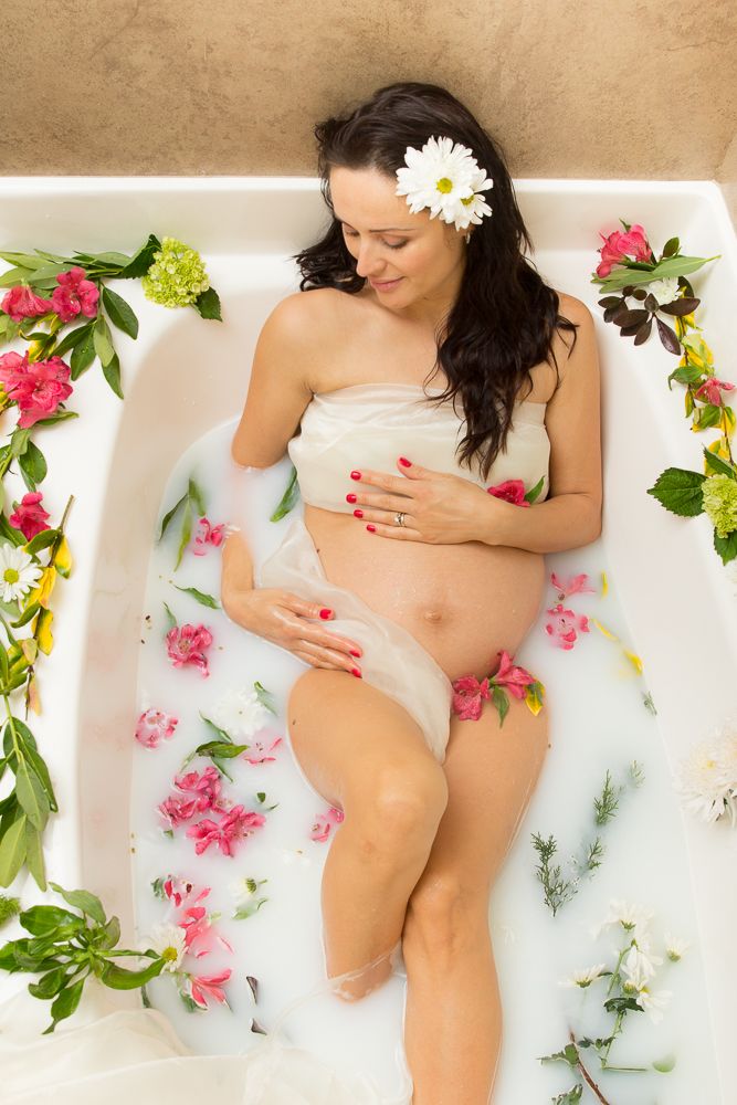 Artistic maternity milk bath photos with pink flowers and white dress.