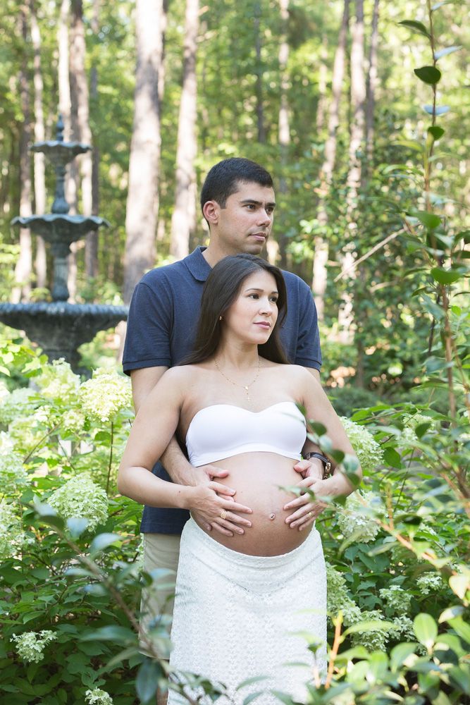 Maternity photoshoot in a lush forest setting with couple posing among trees and greenery.