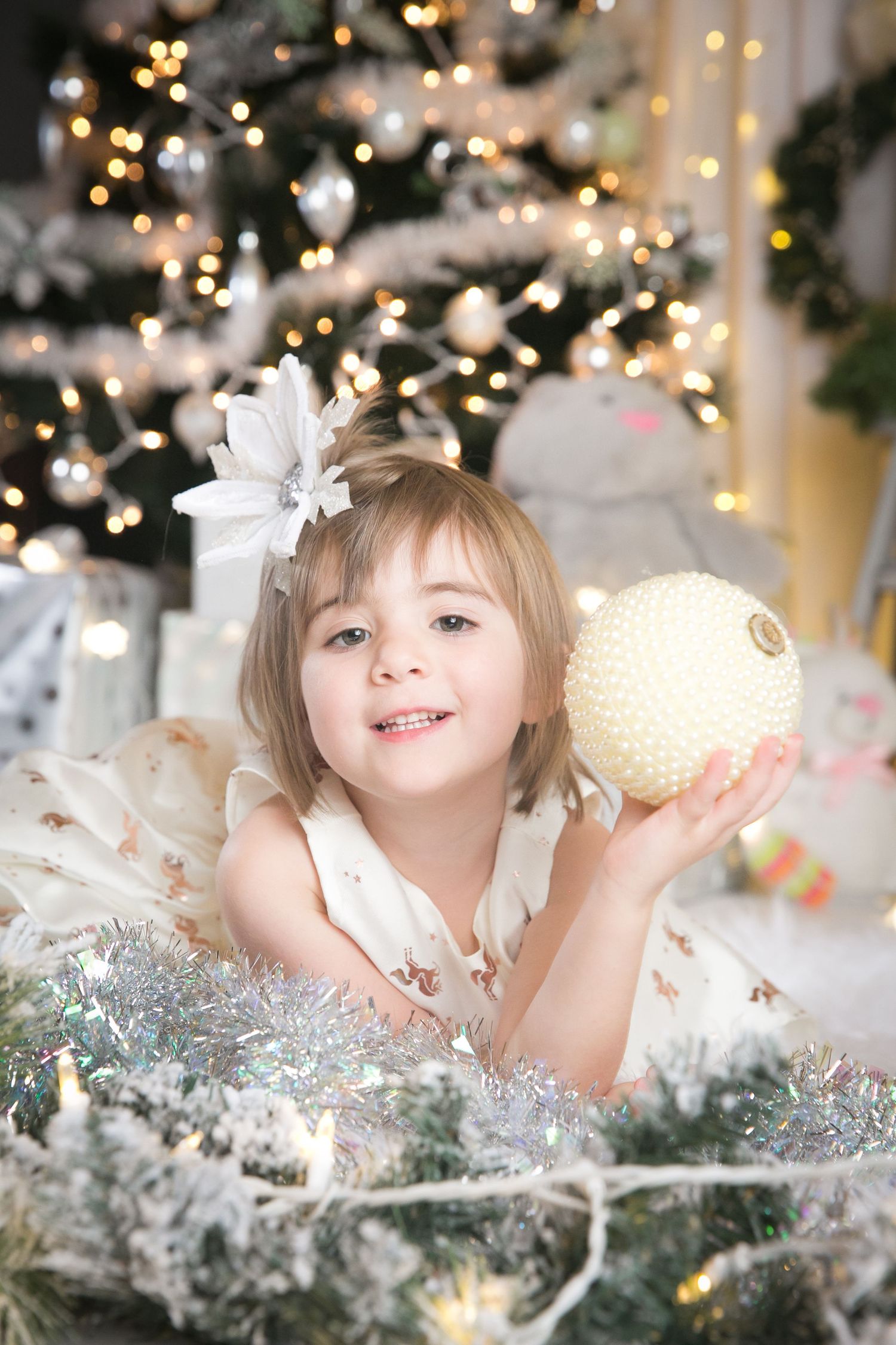 Holiday photo shoot setup with white decorations, bokeh lights, and silver tinsel against a festive backdrop.