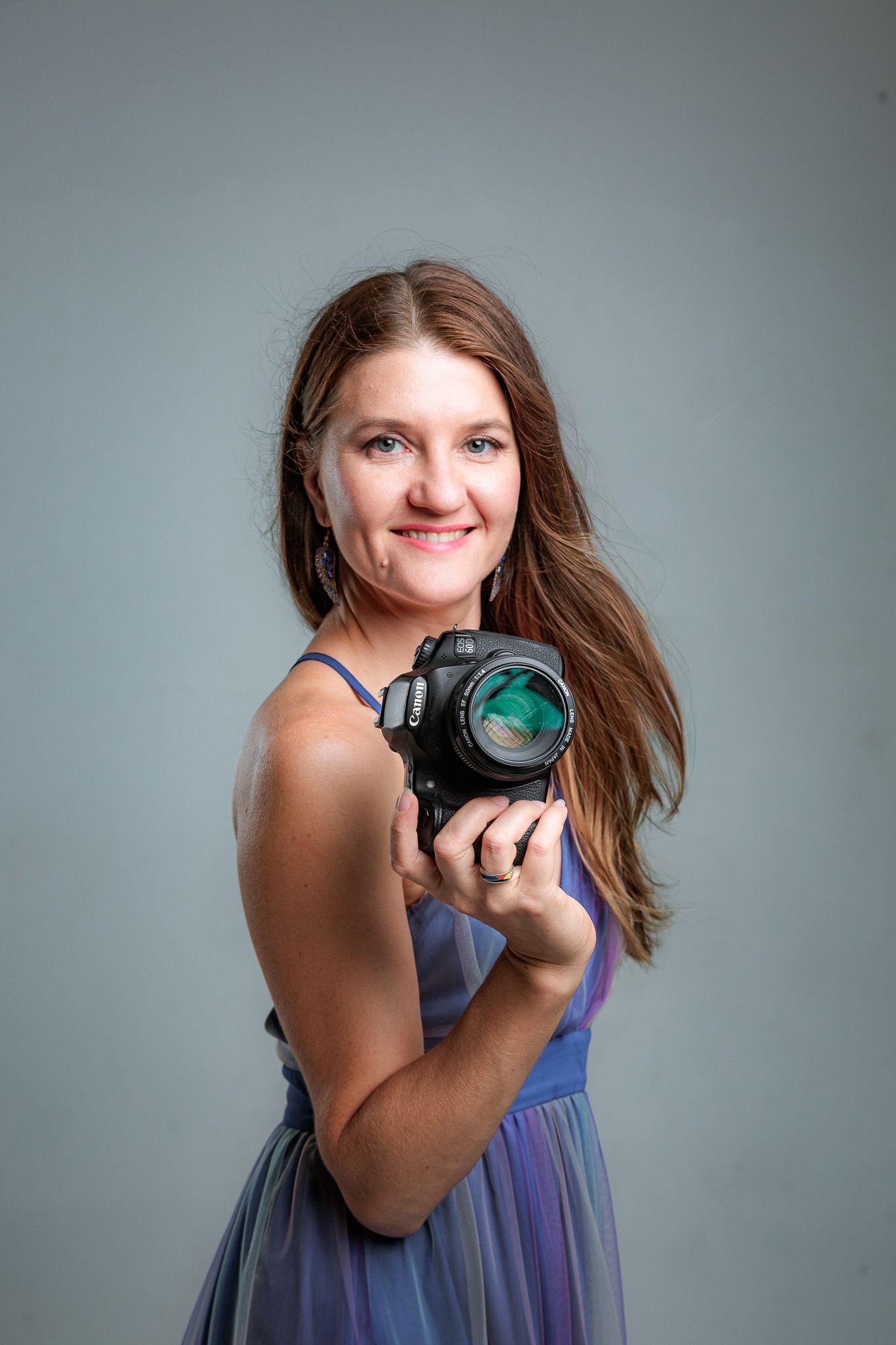 Photographer wearing blue dress demonstrates various camera poses in studio setting.
