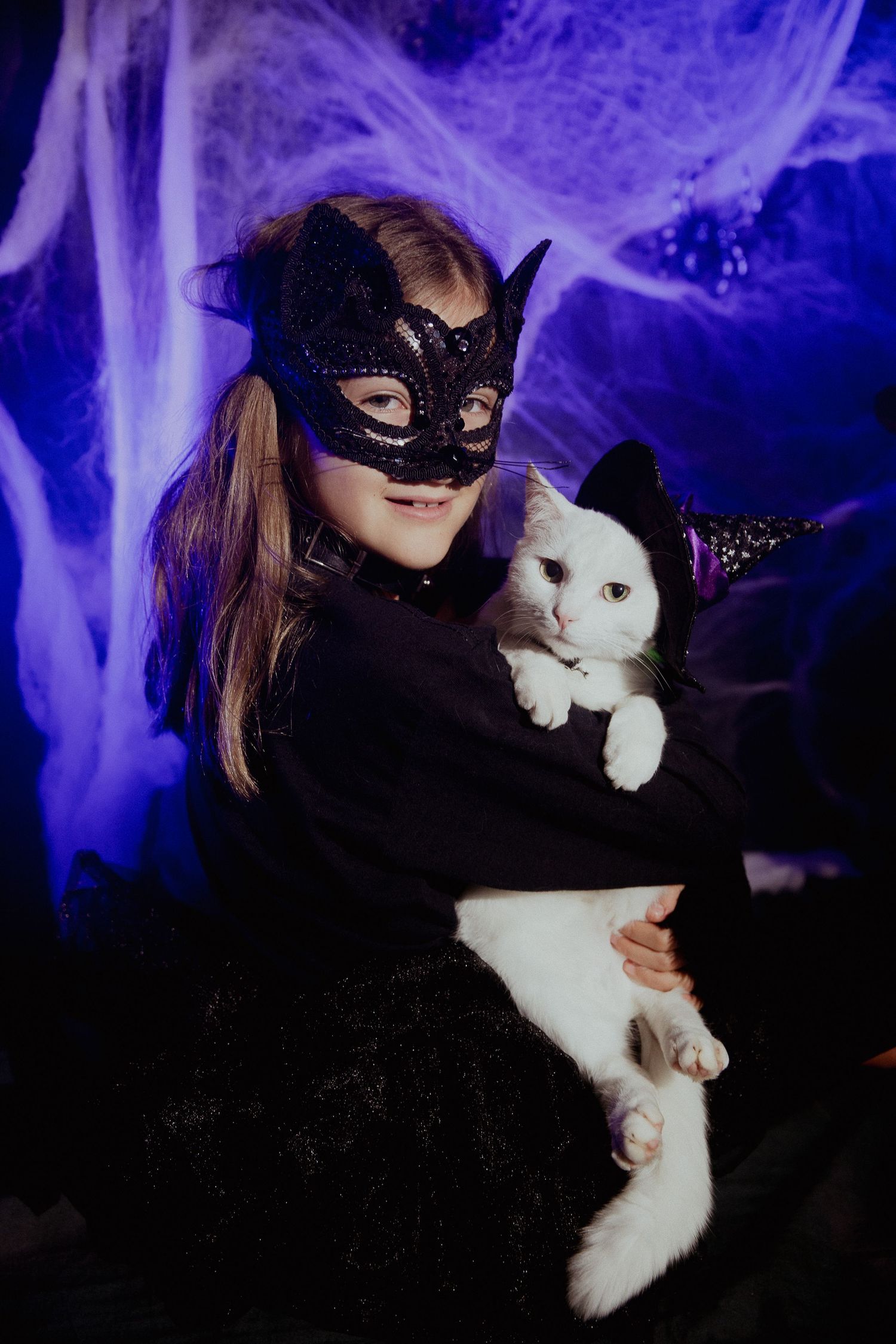 Dramatic portrait with black lace mask and white rabbit against purple-lit spooky backdrop.