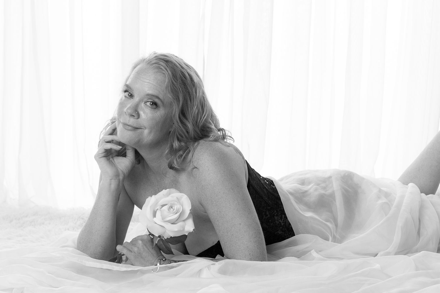 Four artistic black and white boudoir photos showing a woman in romantic poses on white bedding.