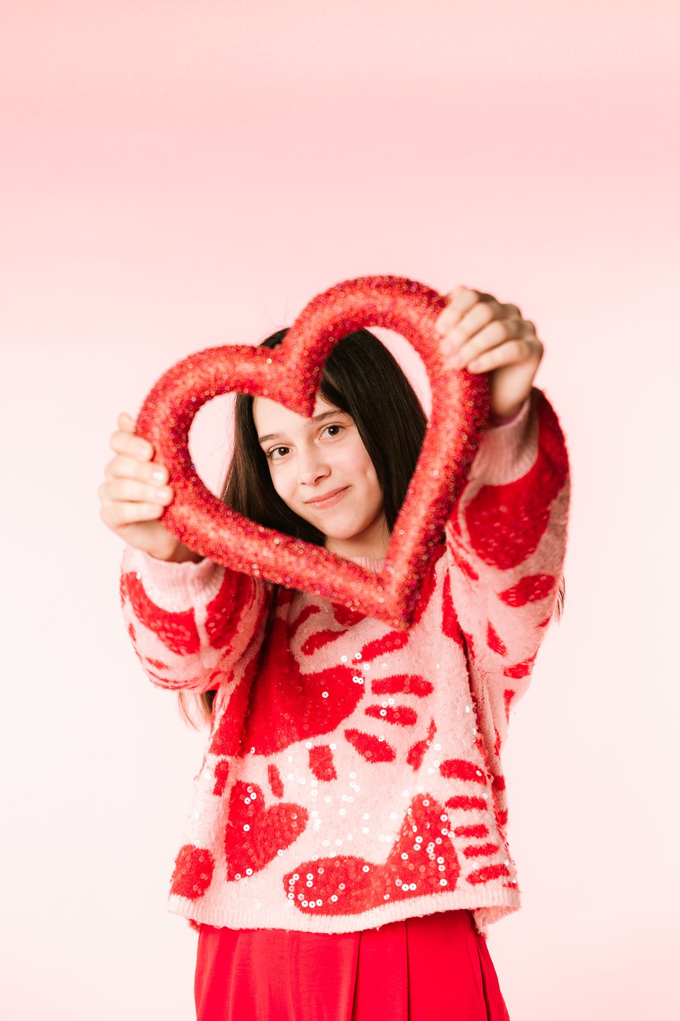 Playful sequence of poses with red fuzzy sweater against pink background.