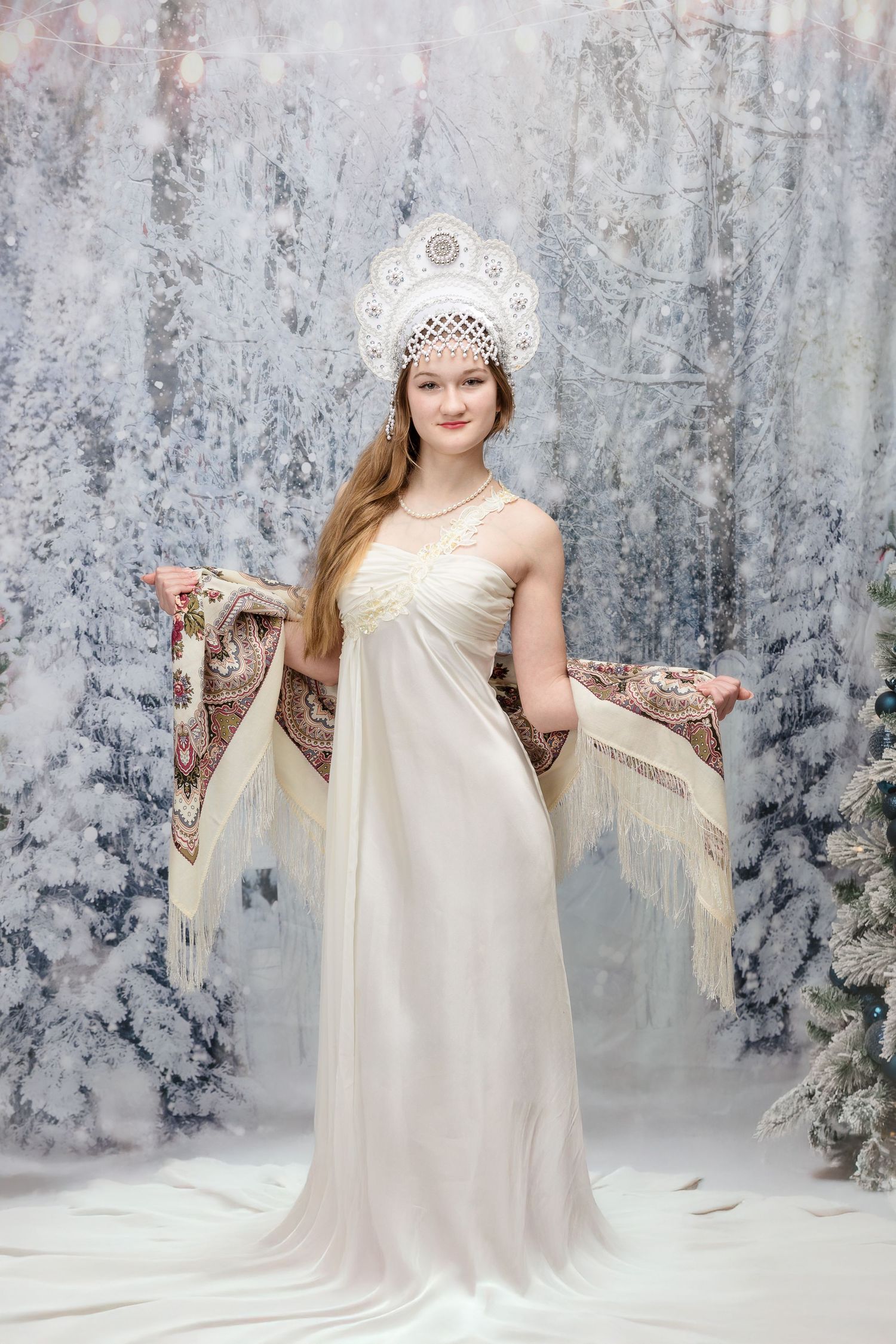Winter themed maternity shoot with white dress and crown against snowy backdrop.