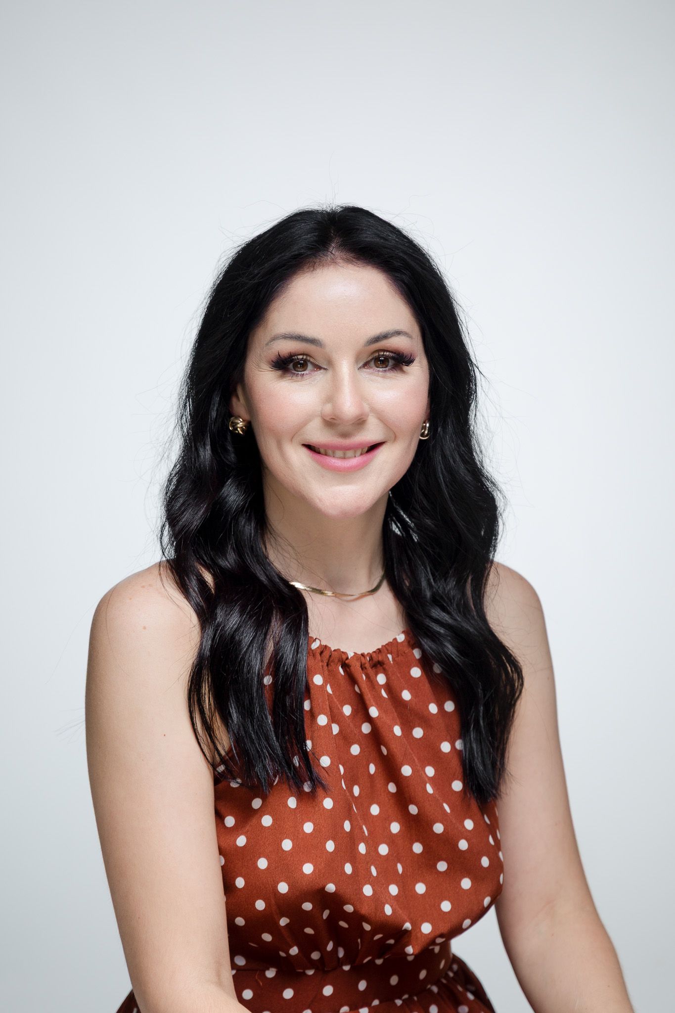 Portrait series against white background wearing brown polka dot sleeveless dress.