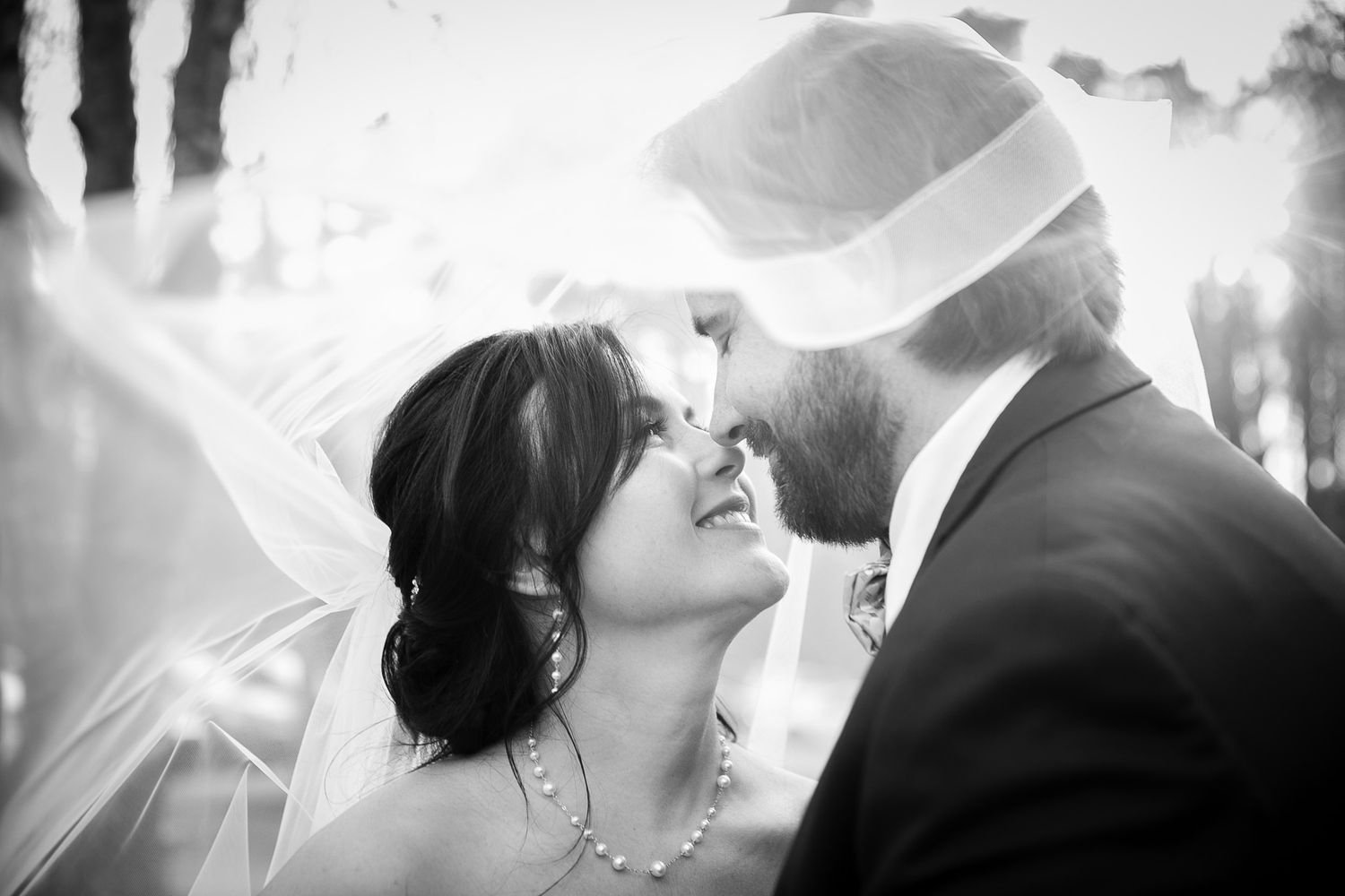Black and white wedding photo of bride and groom sharing a romantic moment under a flowing veil.