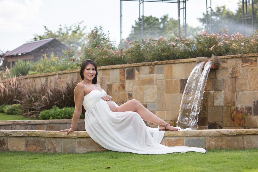 Elegant maternity photos taken at stone garden wall with architectural elements.