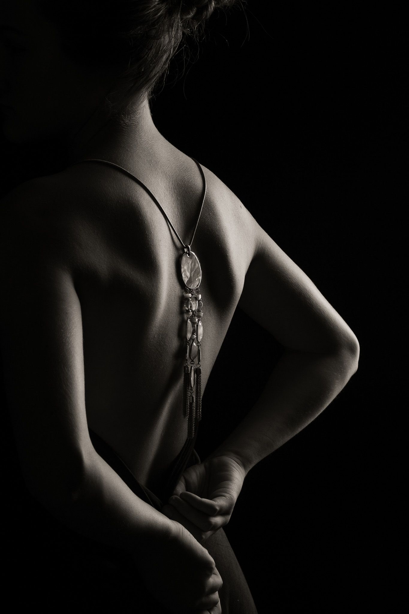 Artistic black and white study of body contours with jewelry in low key lighting.