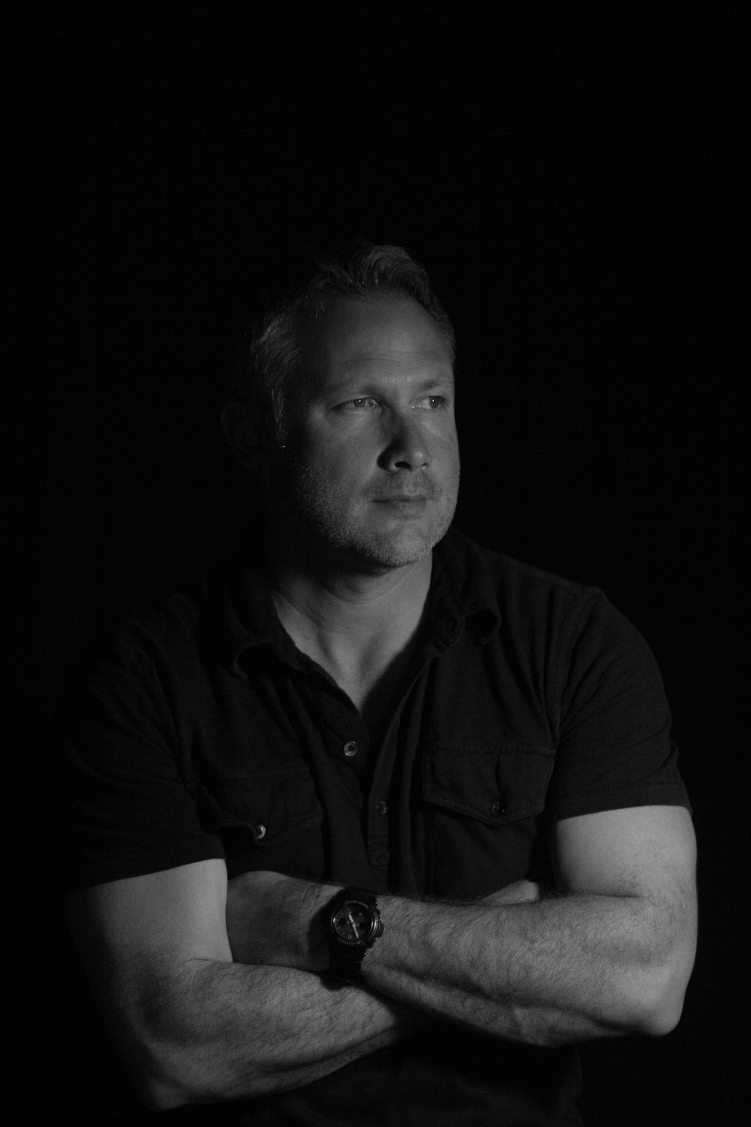 Low key black and white portrait of someone in dark clothing against black background.