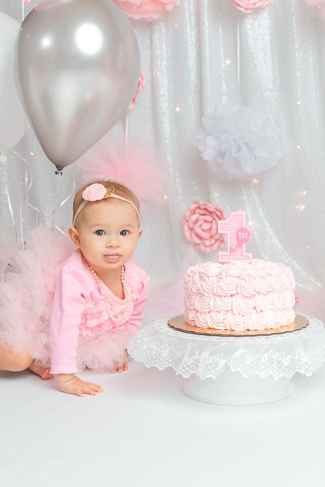 Baby's first birthday setup with pink cake and silver balloons.
