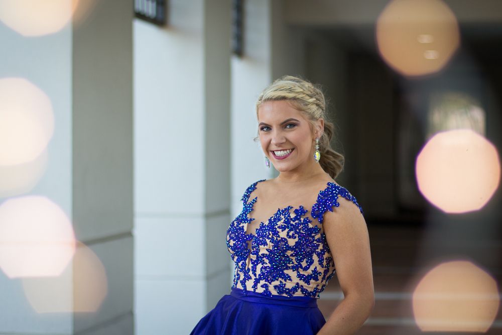 Person in royal blue formal dress with lace details poses in front of white columns.