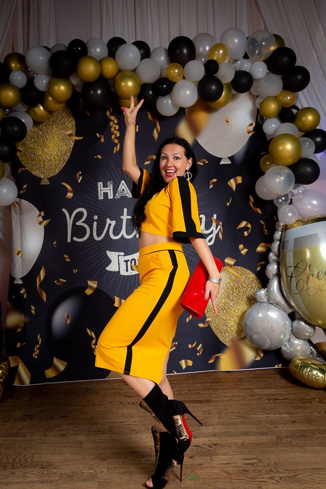 Birthday celebration with black, gold and white balloon arch and confetti.