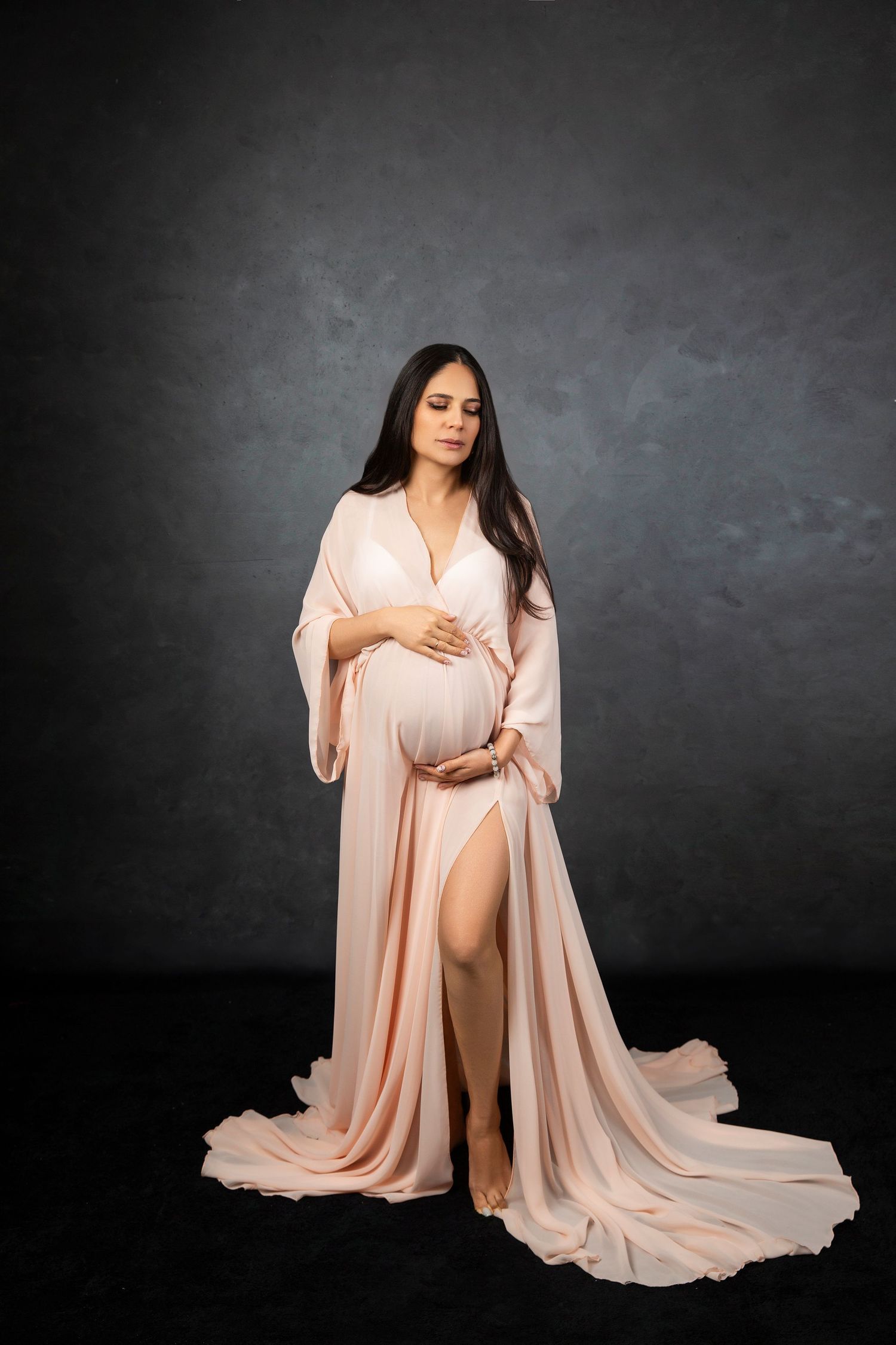 Intimate maternity portrait featuring a draped peach-colored gown against dark background.