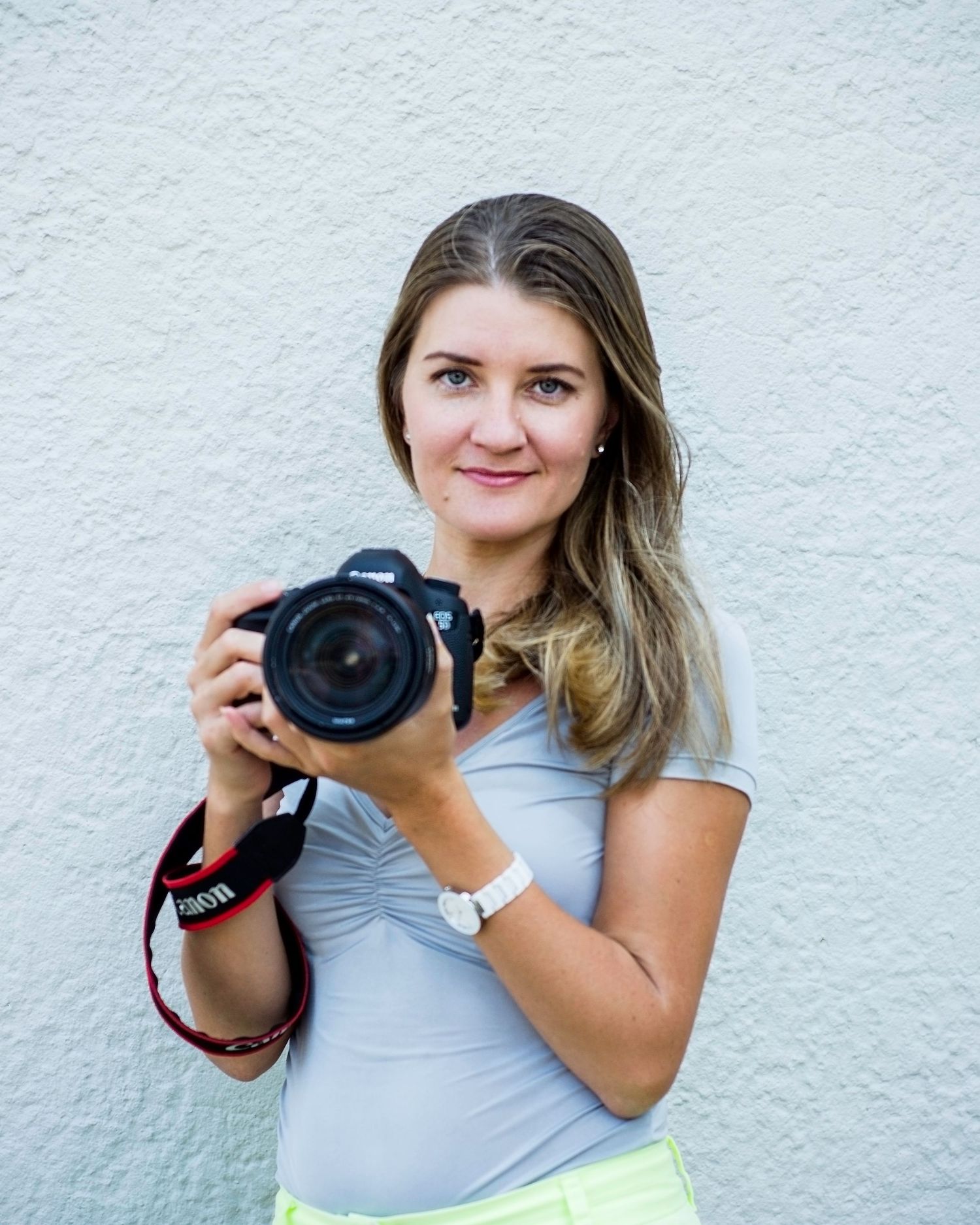 A photographer demonstrates different camera holding positions against a white wall.