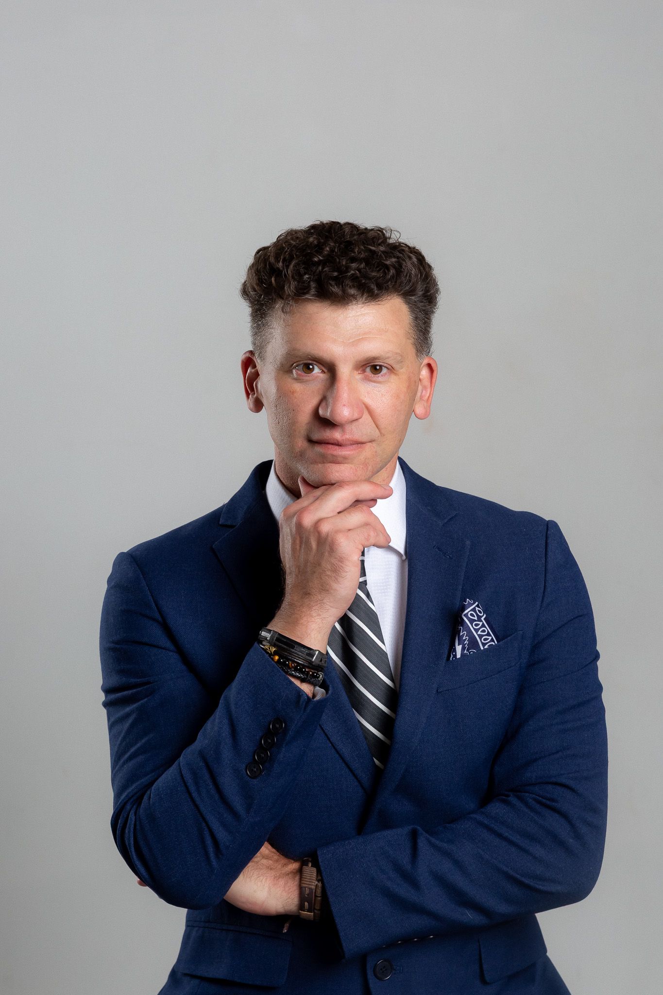 Professional headshot series in navy suit with contemplative poses against grey background.