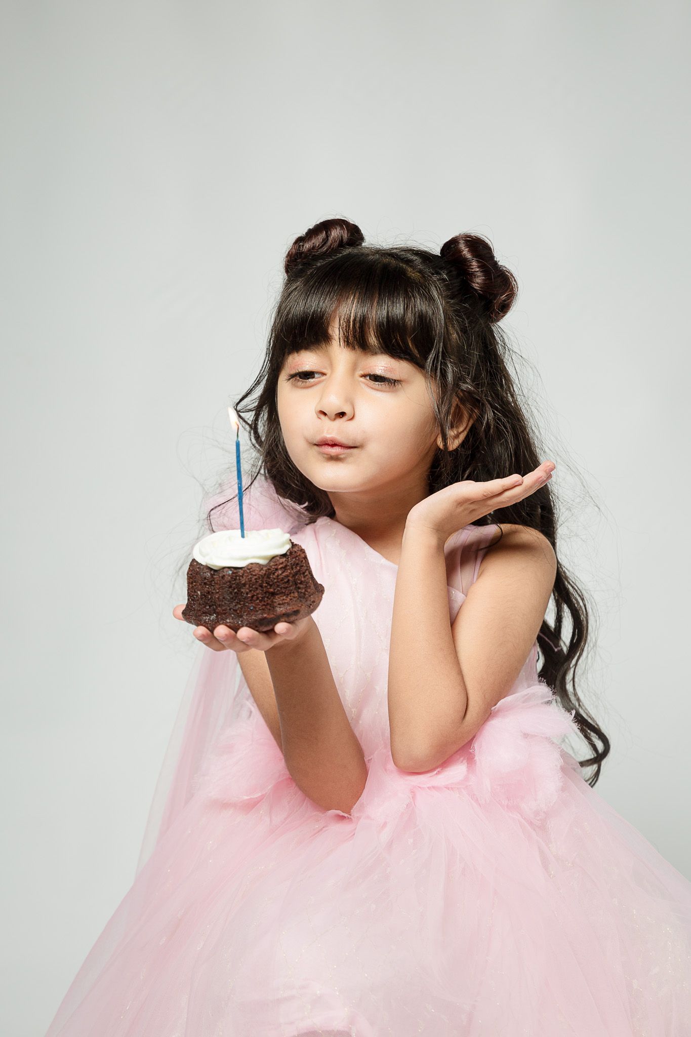 Young girl in pink tutu dress blowing out birthday candle on chocolate cake, celebrating her special day.