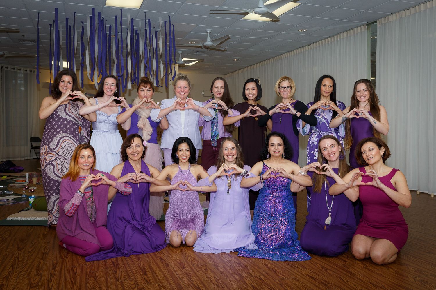 Group photo of people wearing coordinated purple outfits sitting together in a studio setting.