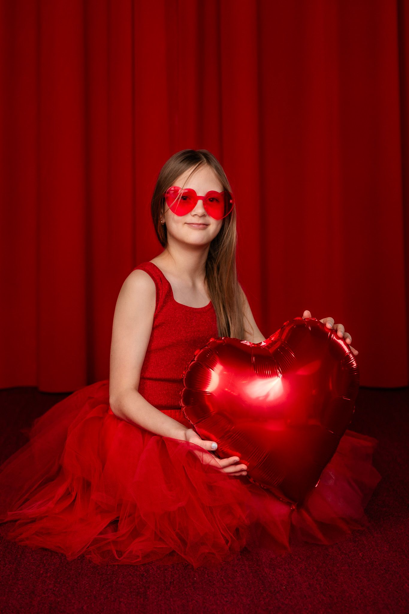 Dramatic red-lit portrait session with heart-shaped props and tulle dress.
