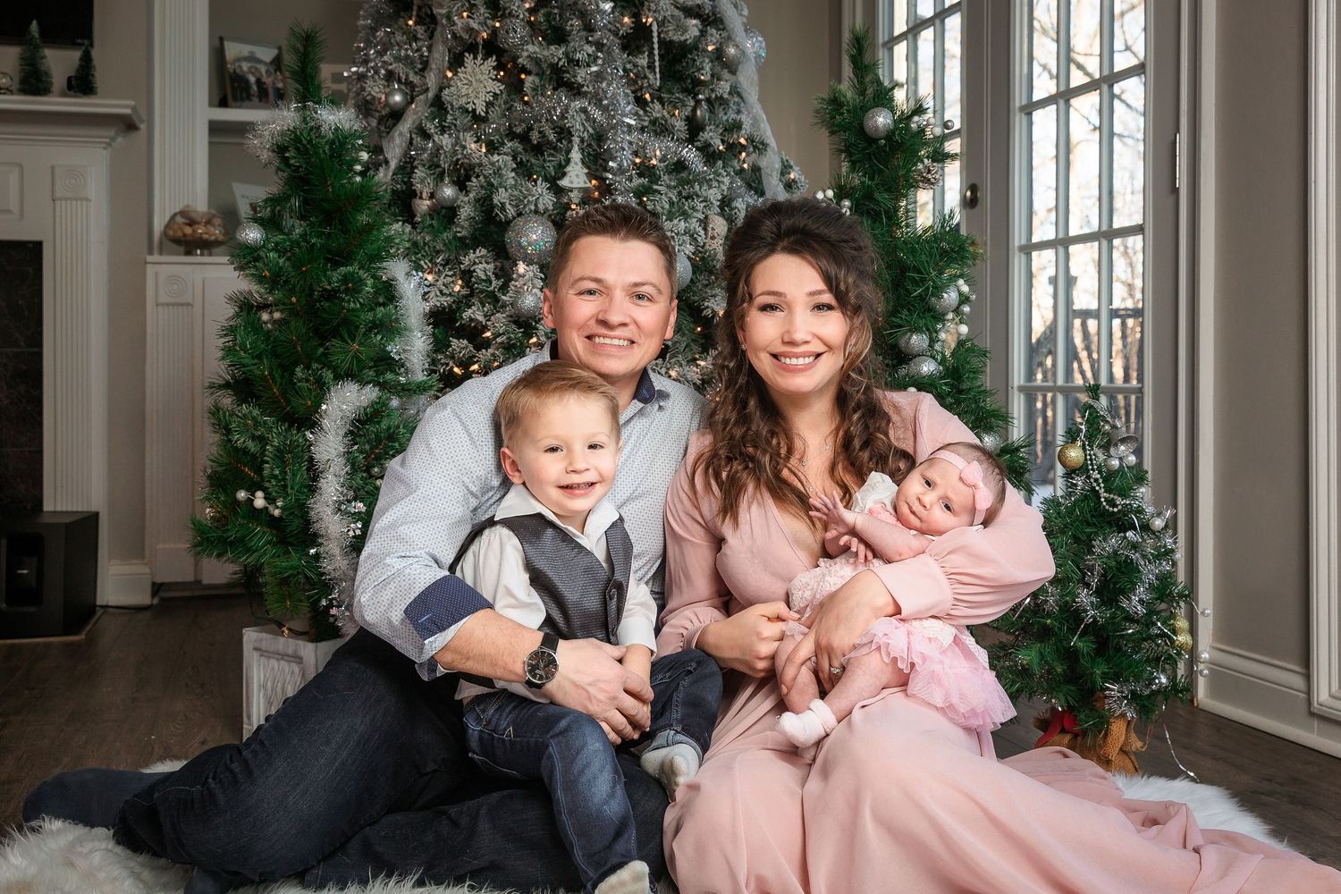 Family portrait session in elegant winter wonderland setting with white decor and Christmas trees.