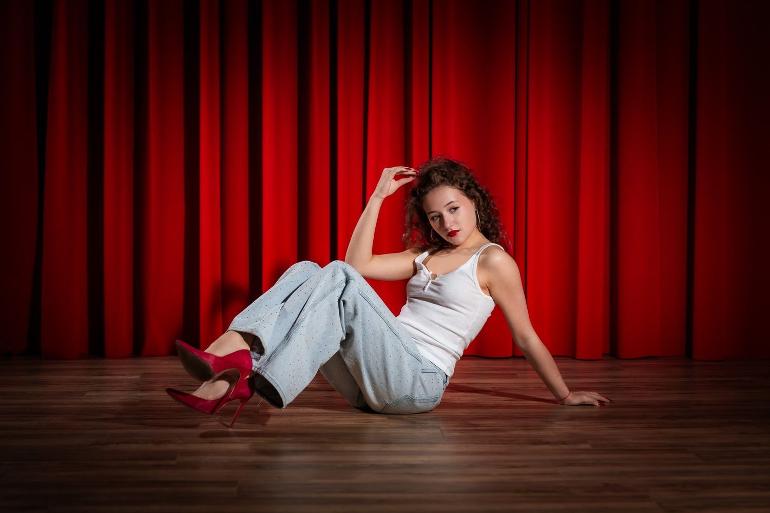 Dramatic poses in white outfit against red stage curtain on wooden floor.