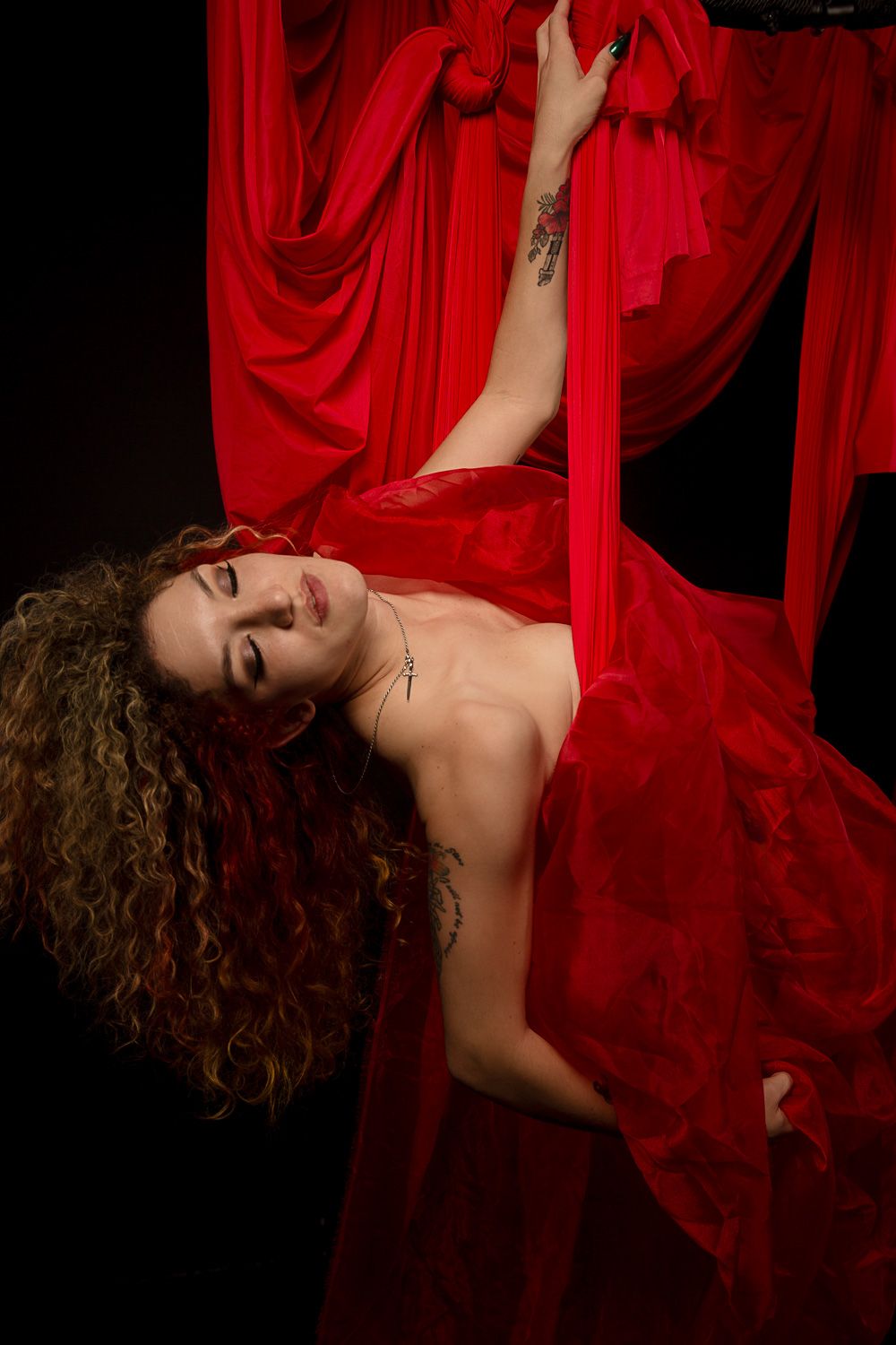 Dramatic aerial dance poses with billowing red fabric in dark studio setting.