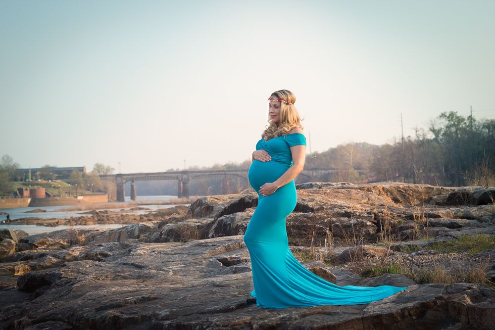 Dramatic maternity portraits on rocky landscape with flowing teal dress catching wind.
